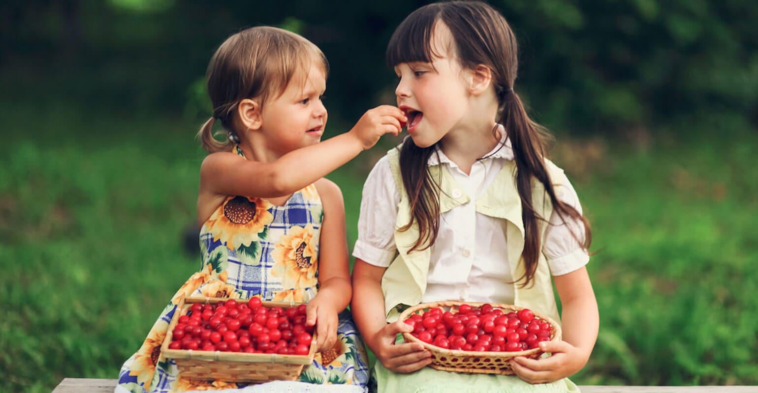 Two young girls eating cherries.