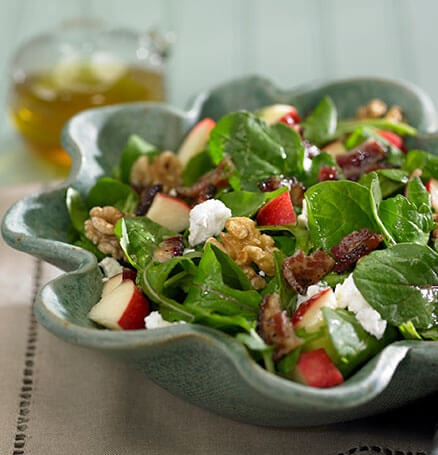 A unique-looking blue bowl full of candied-bacon apple salad with oil.