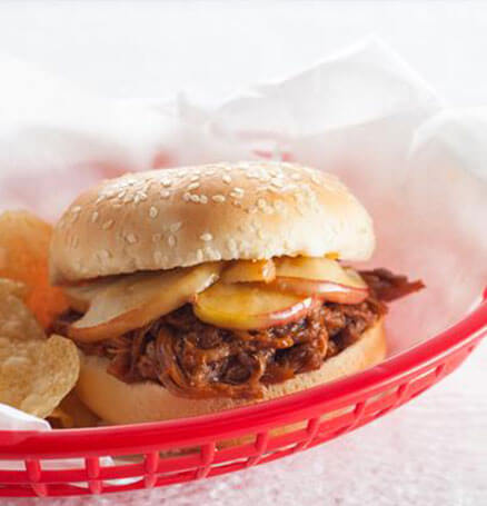 Expertly-prepared apple-flavored BBQ sandwich in red basket with potato chips.
