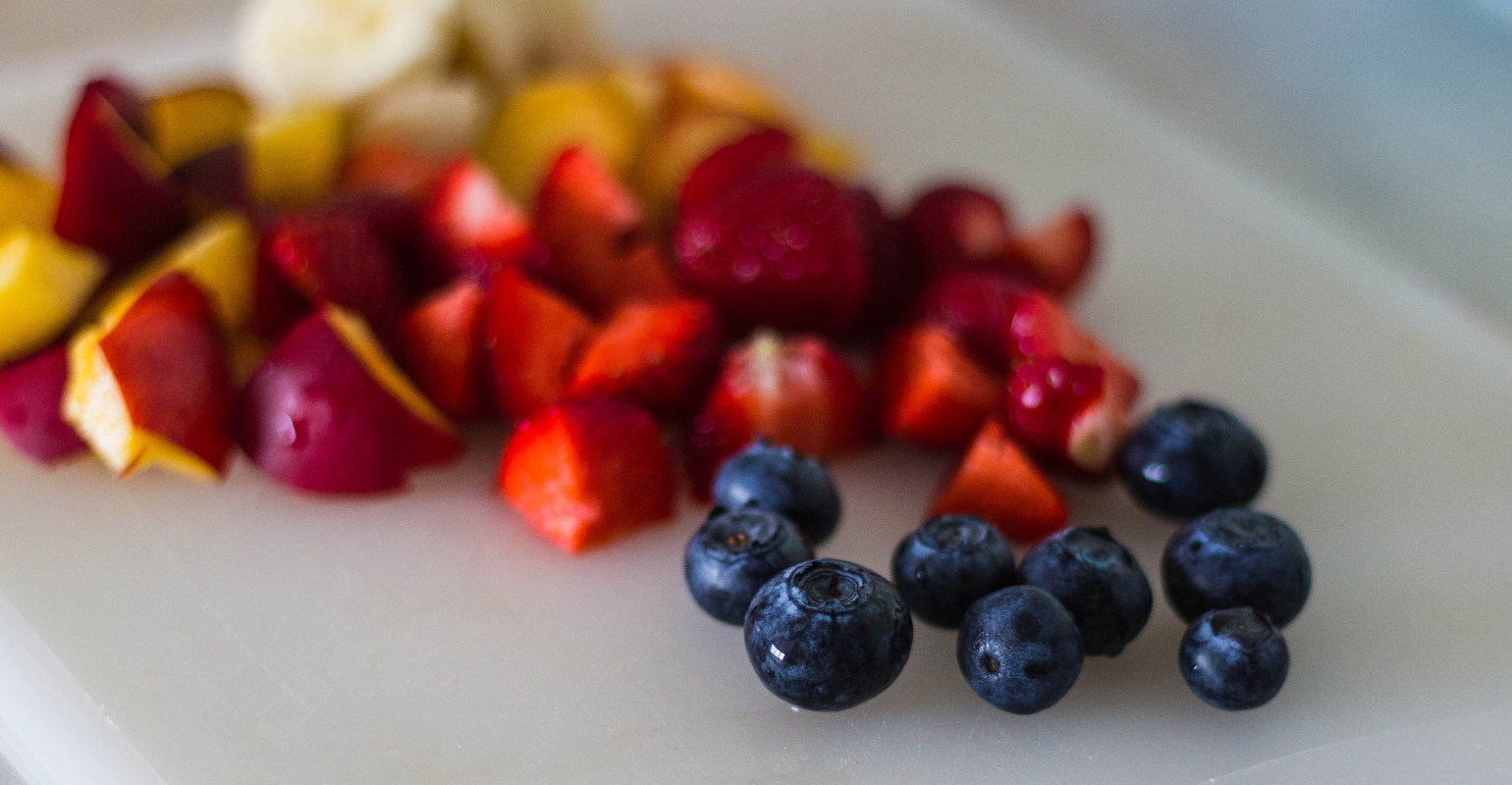 A delicious looking array of diced apples, strawberries, and whole blueberries on a cutting board.